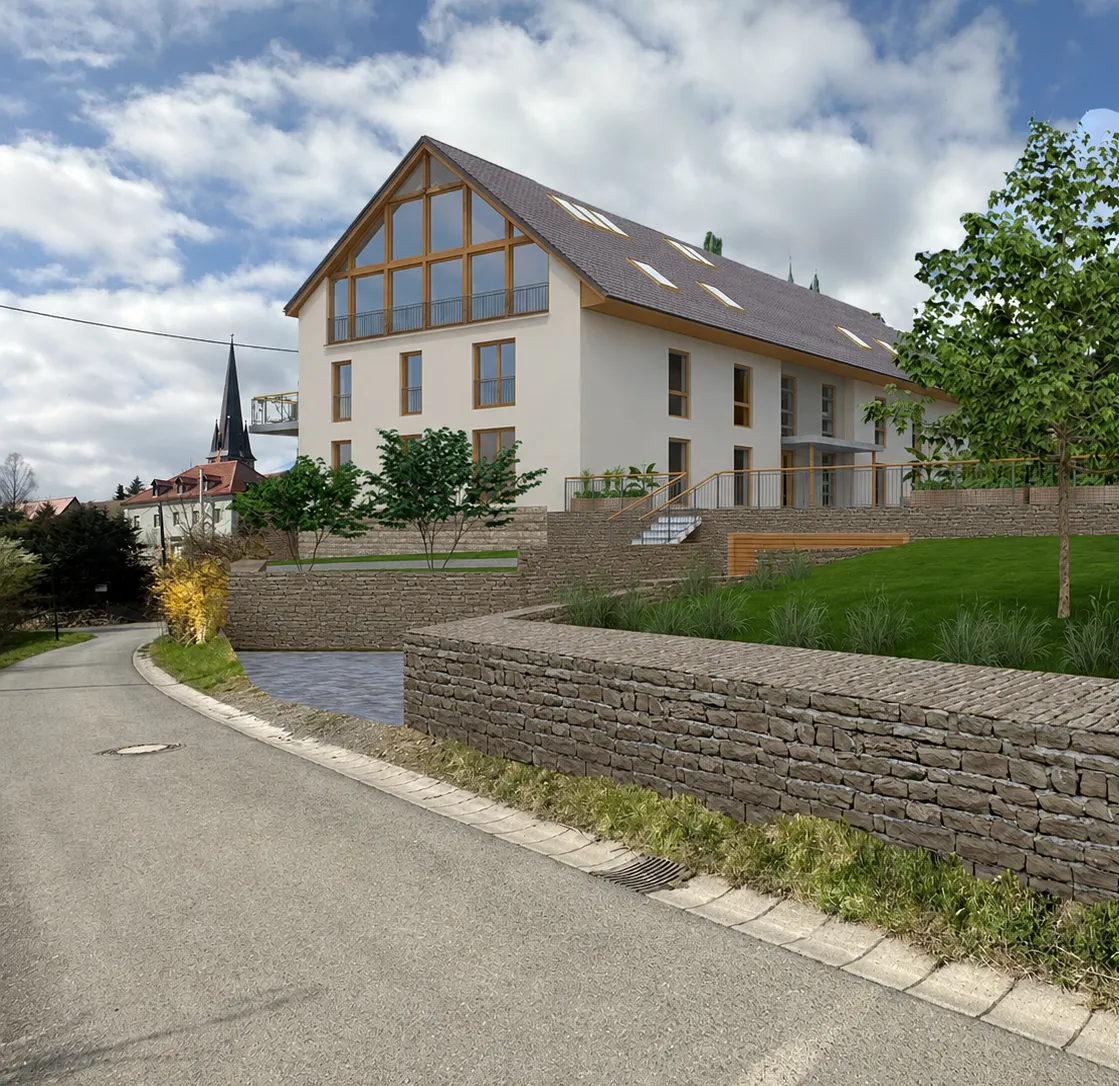 Mehrfamilienhaus mit verglastem Giebel über Natursteinmauern und Rasenflächen, im Hintergrund der Kirchturm des Ortes